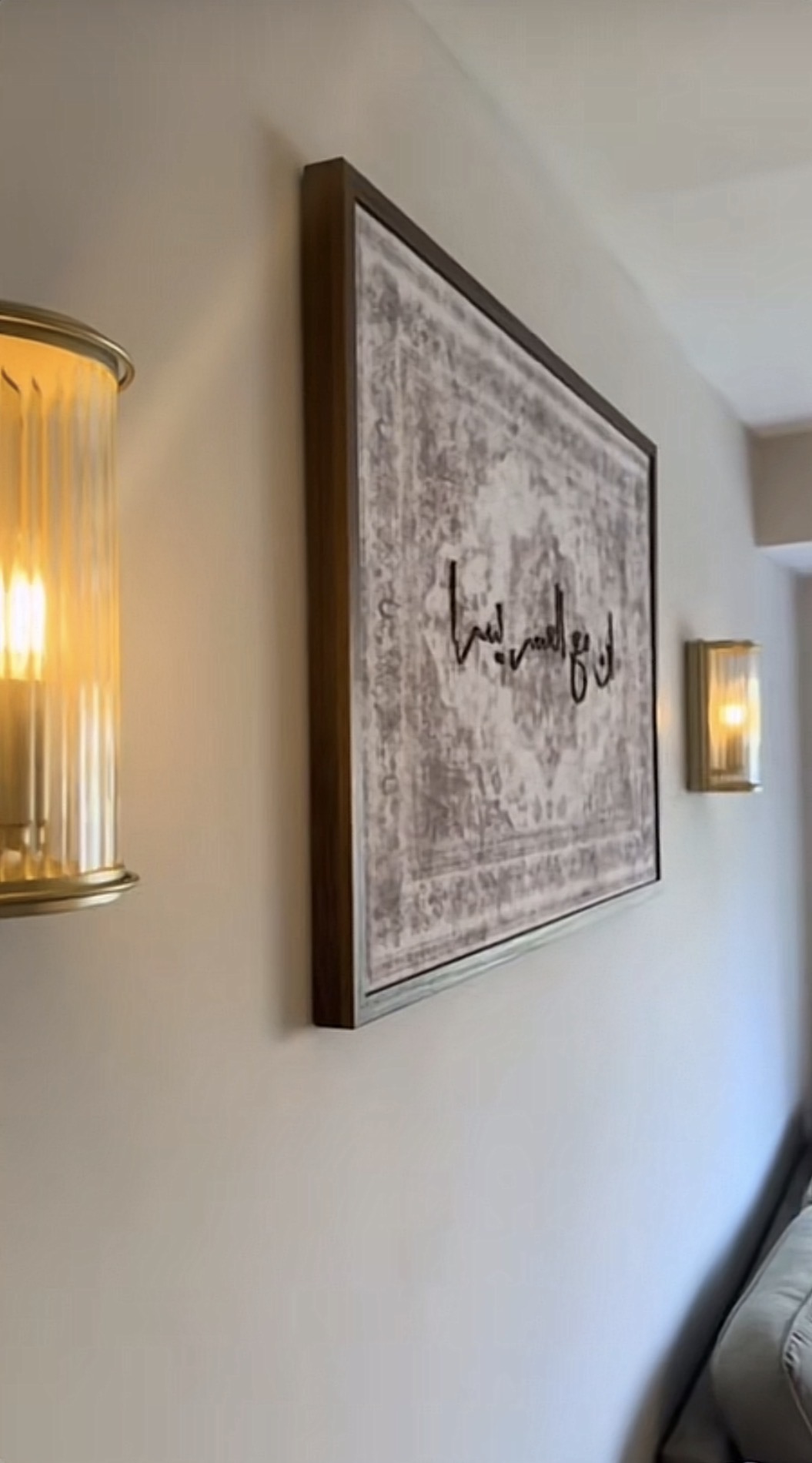 Framed Islamic calligraphy on a warm cream wall flanked by gold sconces